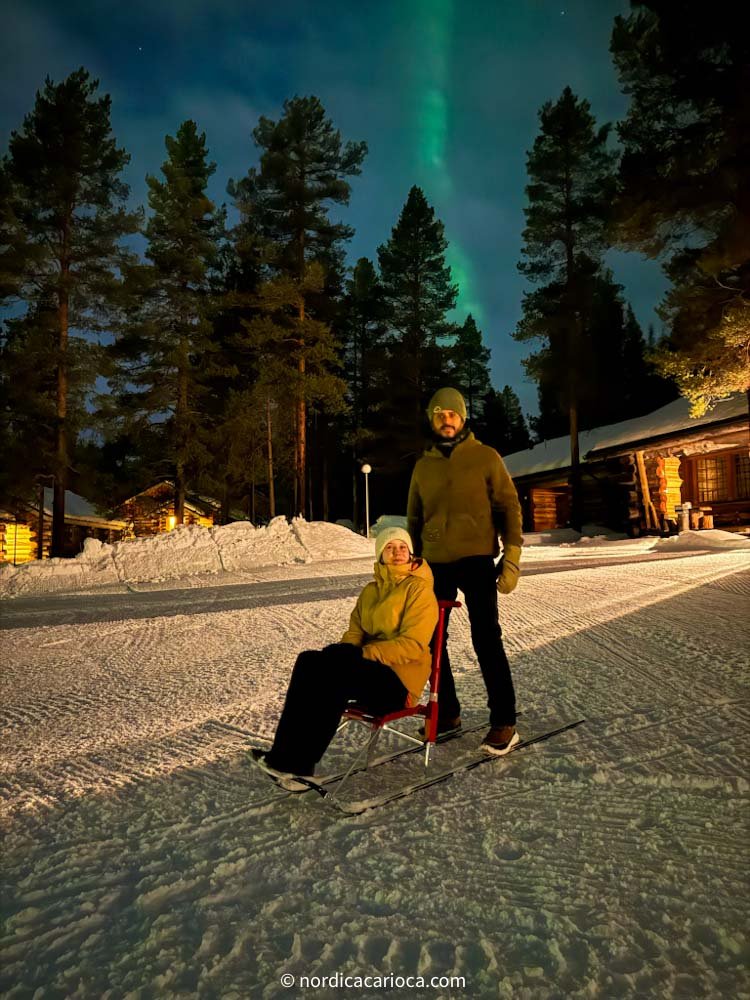 A couple in Finnish Lapland with sledge and aurora borealis behind